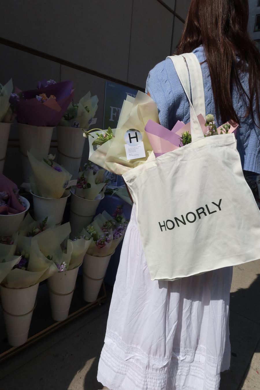 Someone walking away with flowers in an Honorly tote bag.