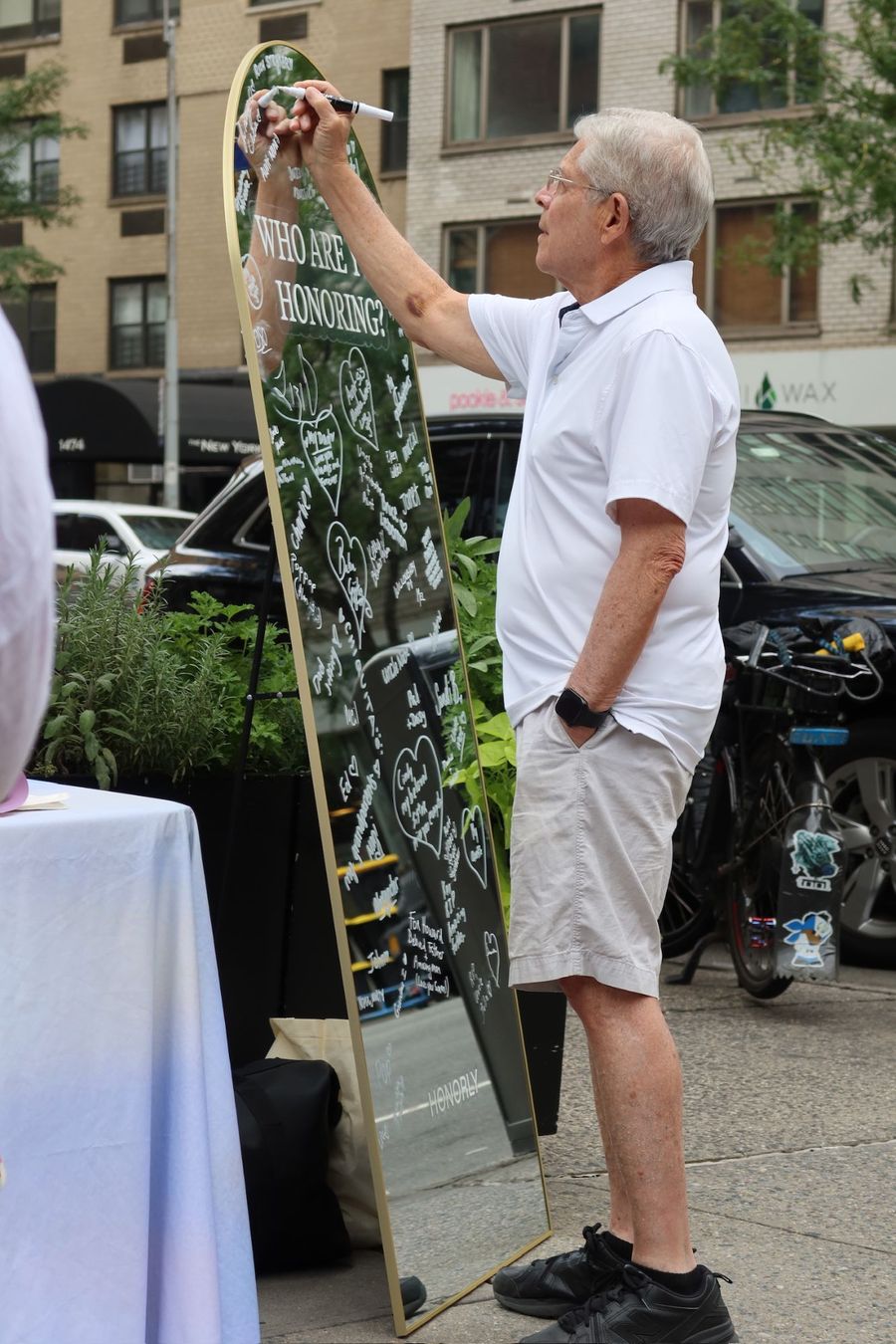 A man writing on a standing mirror headed Who are you honoring?